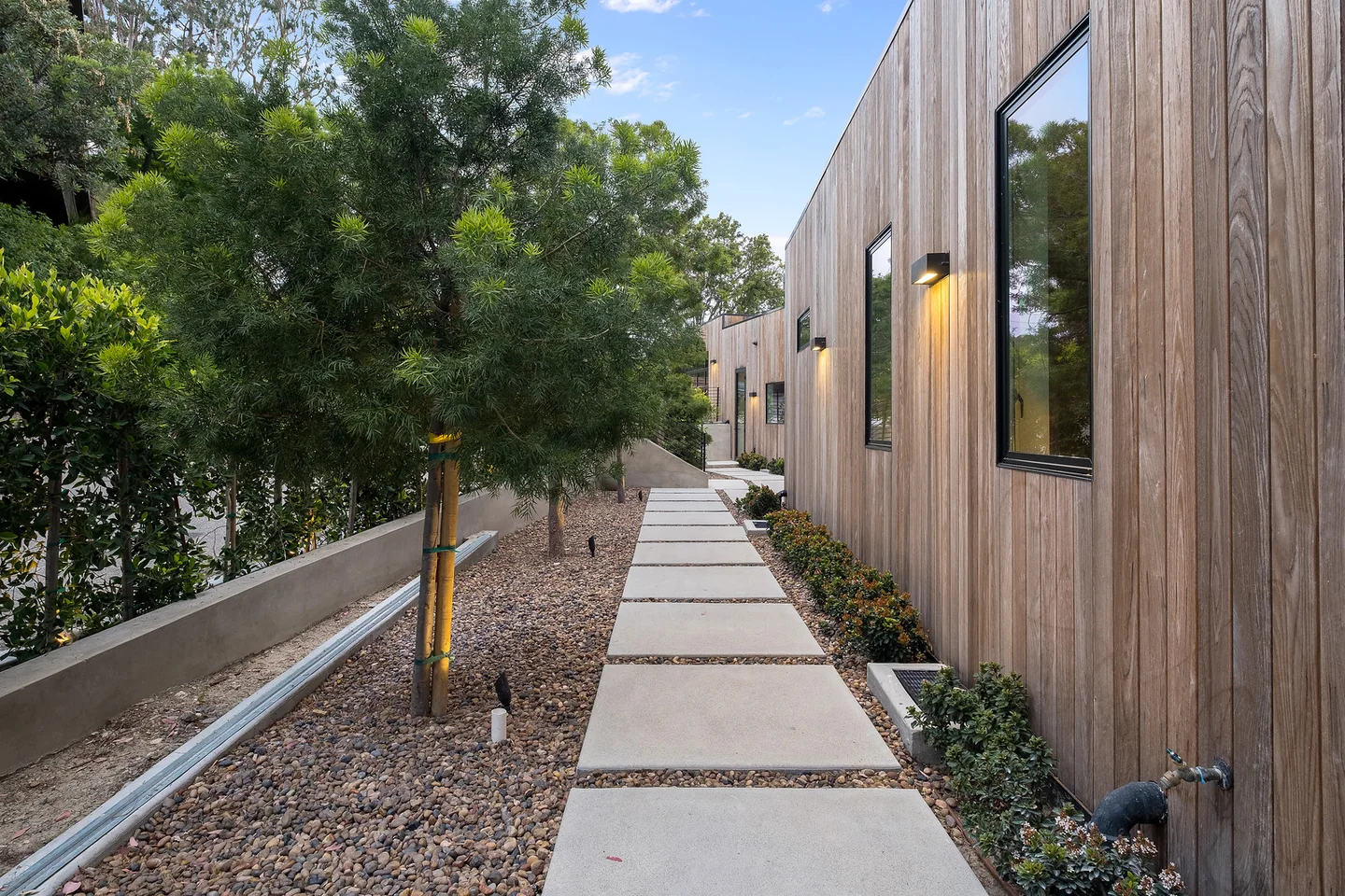 Narrow stepped path beside the timber-clad Dixie Canyon residence, with a guardrail above the sloping tree-lined site.