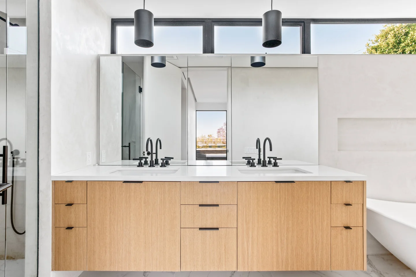 Halderman double vanity with timber drawer fronts, three mirrors, slender pendant lights and dark wall-mounted taps.