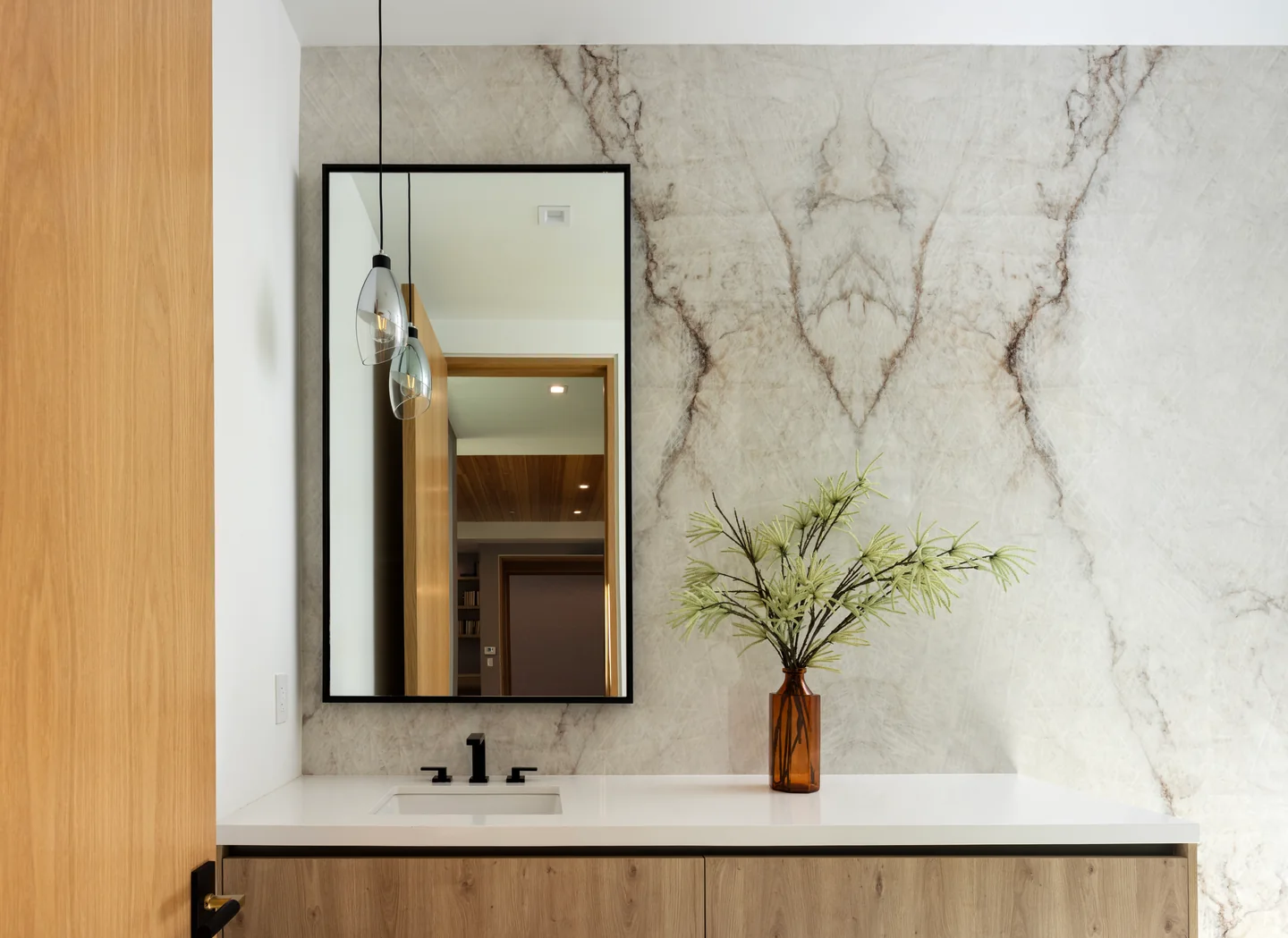 Chalon Road vanity with a tall rectangular mirror, veined stone wall, inset basin and adjoining timber panel.