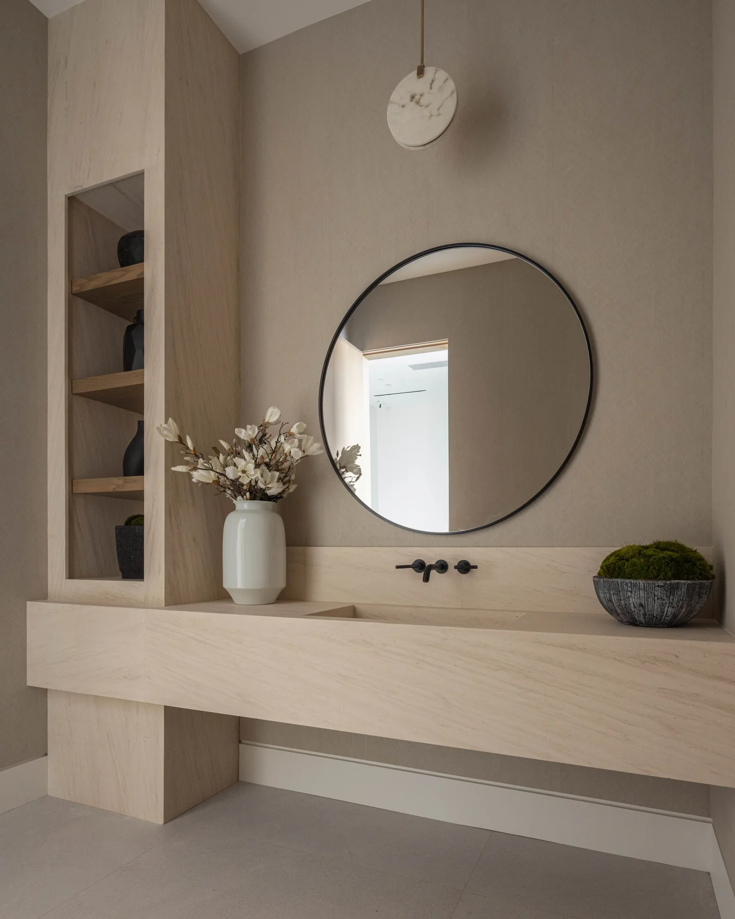 Petit Avenue powder room with a pale fitted vanity, round mirror and recessed shelves at the side.