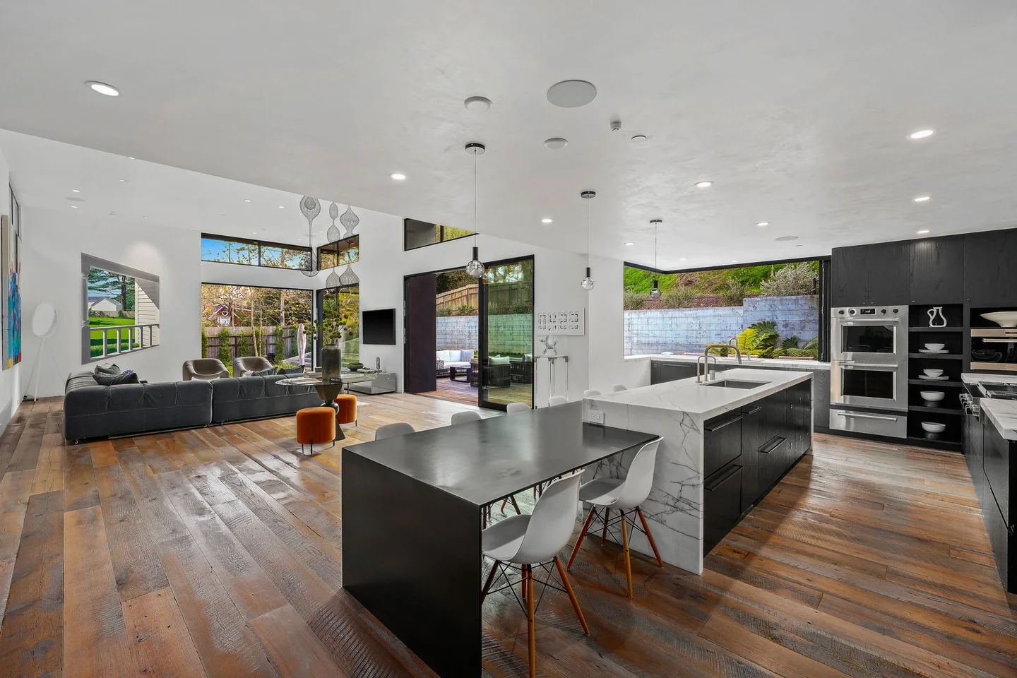 Rivas Canyon kitchen with a dark island, timber floor and open views through the adjoining living and dining spaces.