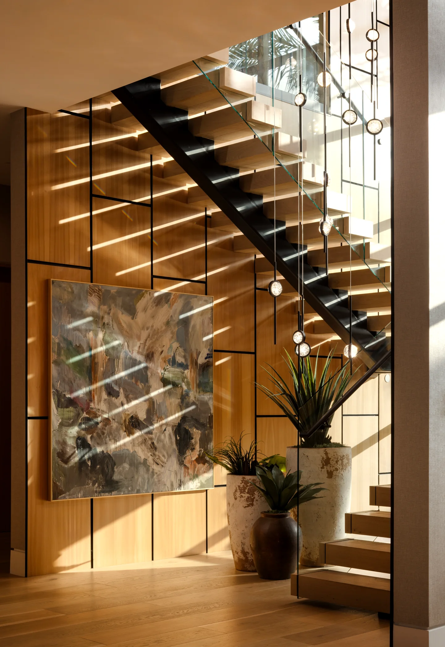 Open staircase with timber treads, glass balustrades and pendant lights beside tall glazing.