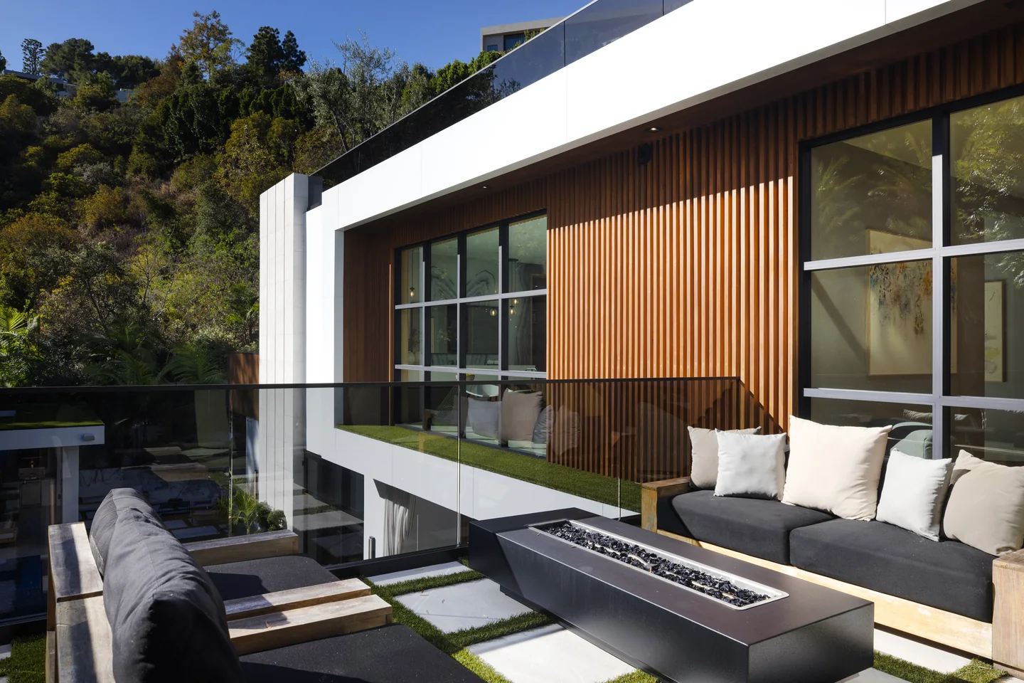 Glazed doors open onto a balcony with a fire table beneath a timber-clad upper facade.