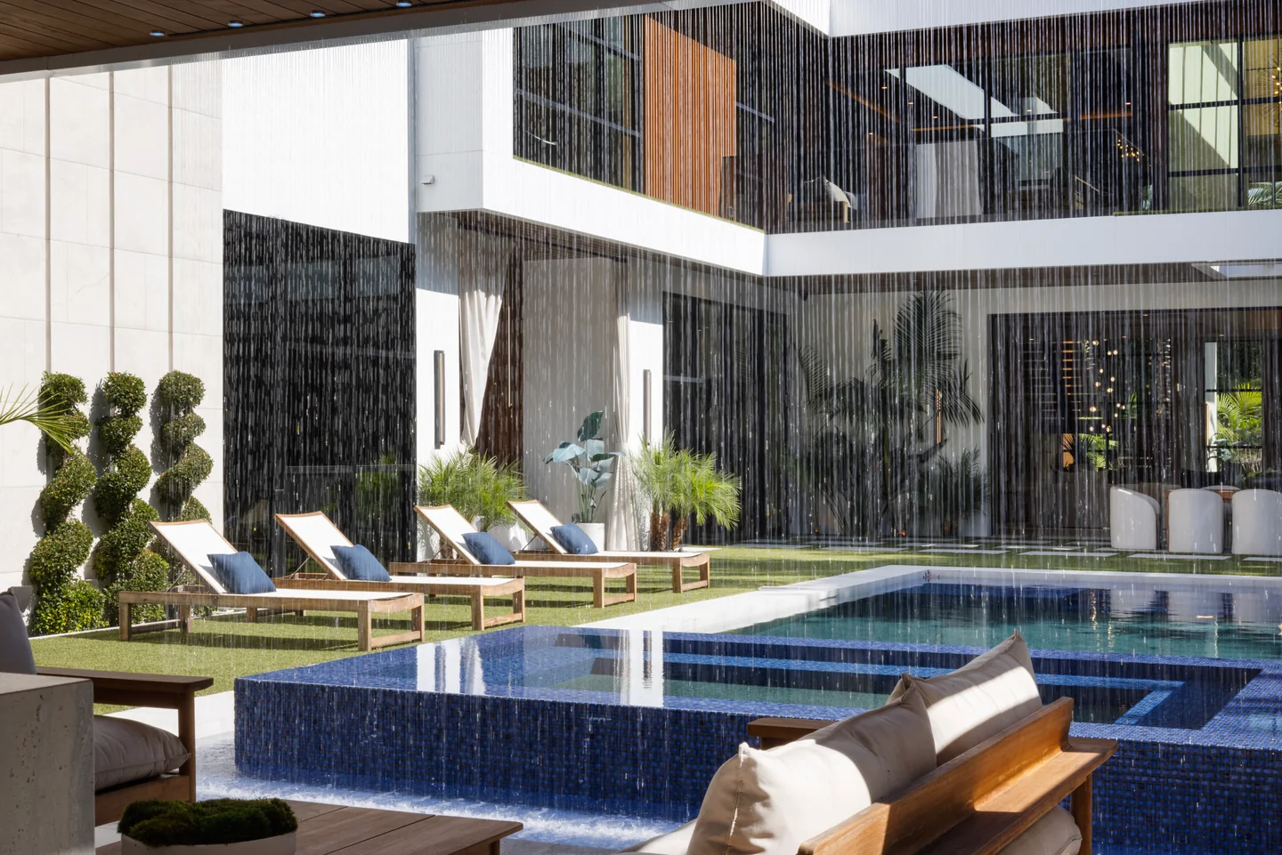 Pool and sunken seating beside the glazed rear facade, with water falling from the upper edge.