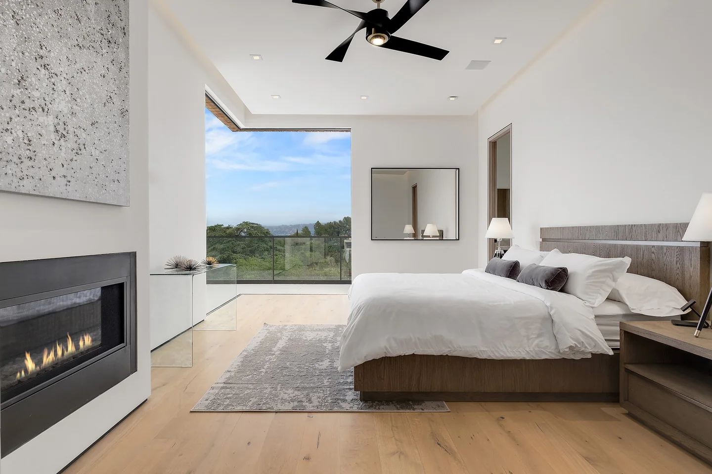 Primary bedroom with a textured fireplace wall and broad glazing opening to a hillside terrace.