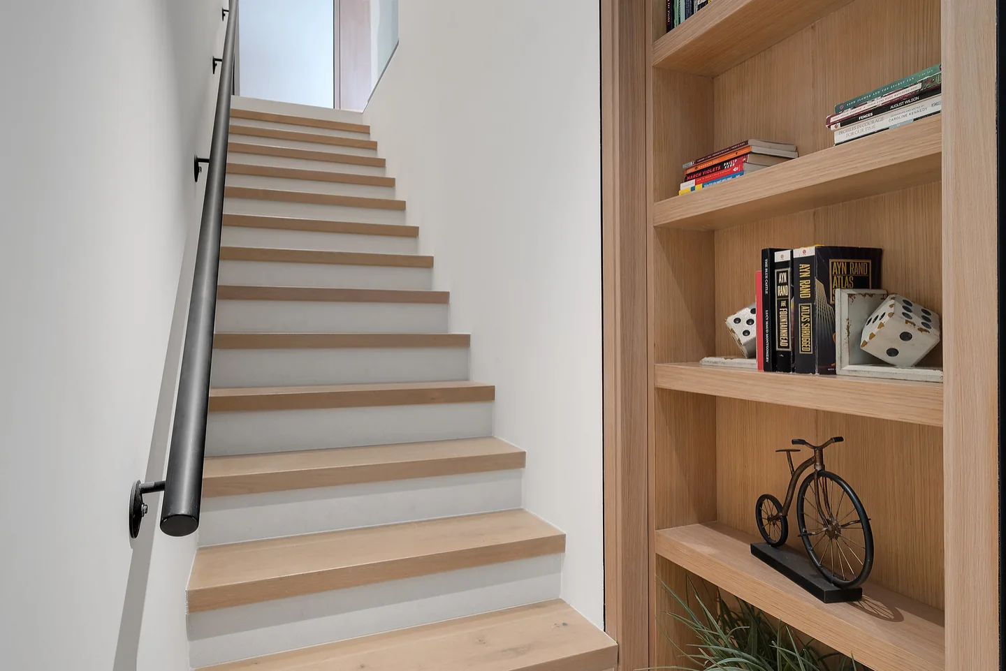 Timber stair rises beside a built-in bookshelf and a dark handrail.