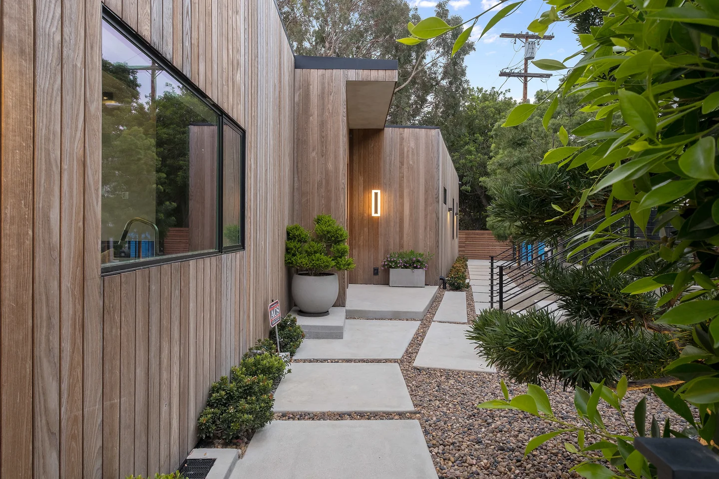 Planted entry path beside timber-clad walls and an orange-framed entrance door.