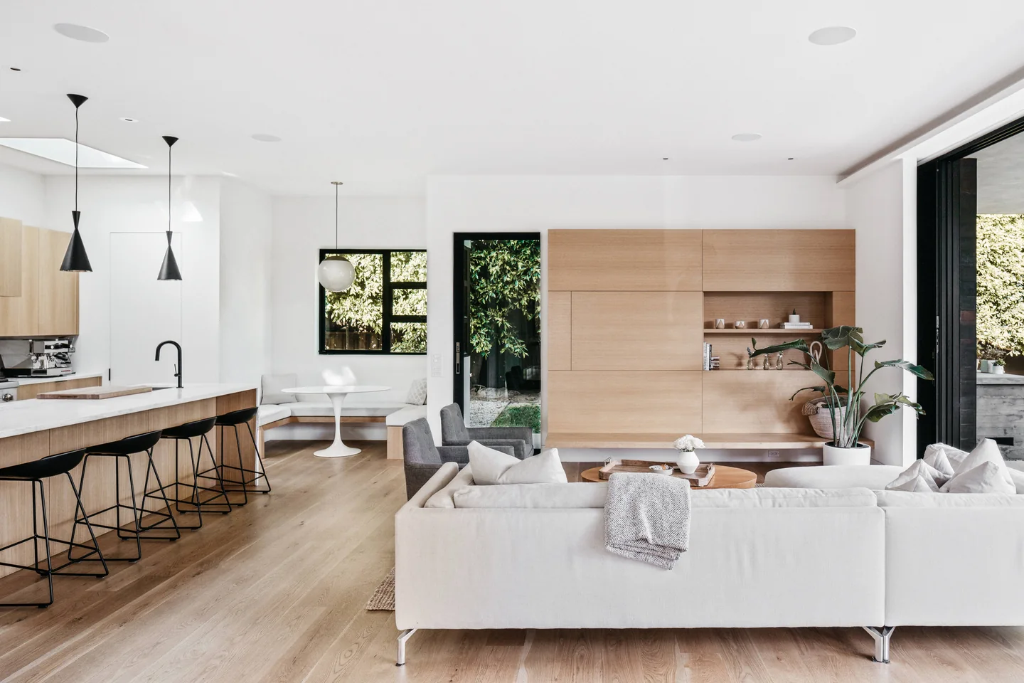 Open living room with timber kitchen cabinetry, a linear fireplace and garden-facing glazing.