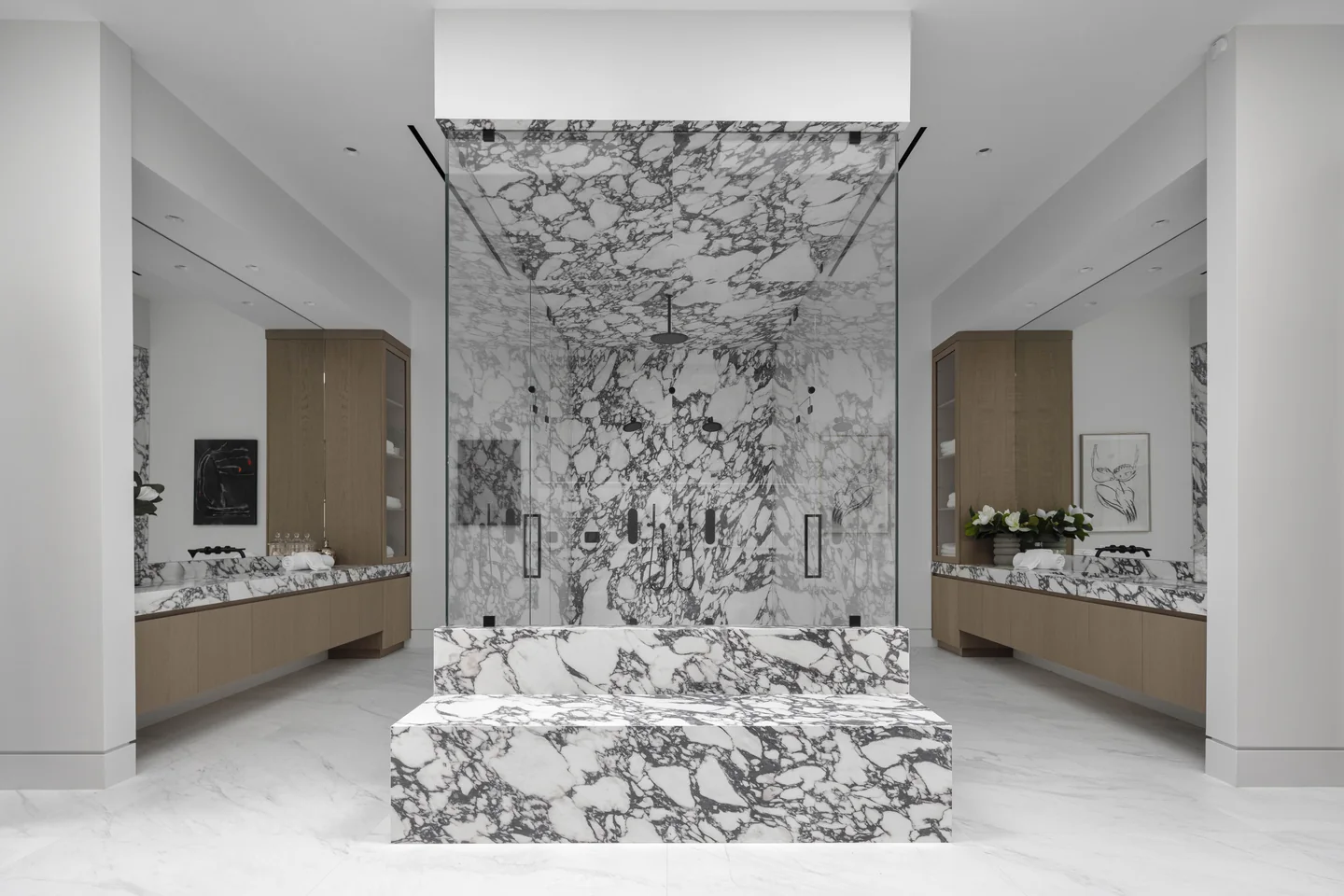 Veined freestanding bath aligned with a broad stone shower wall and flanking vanities.