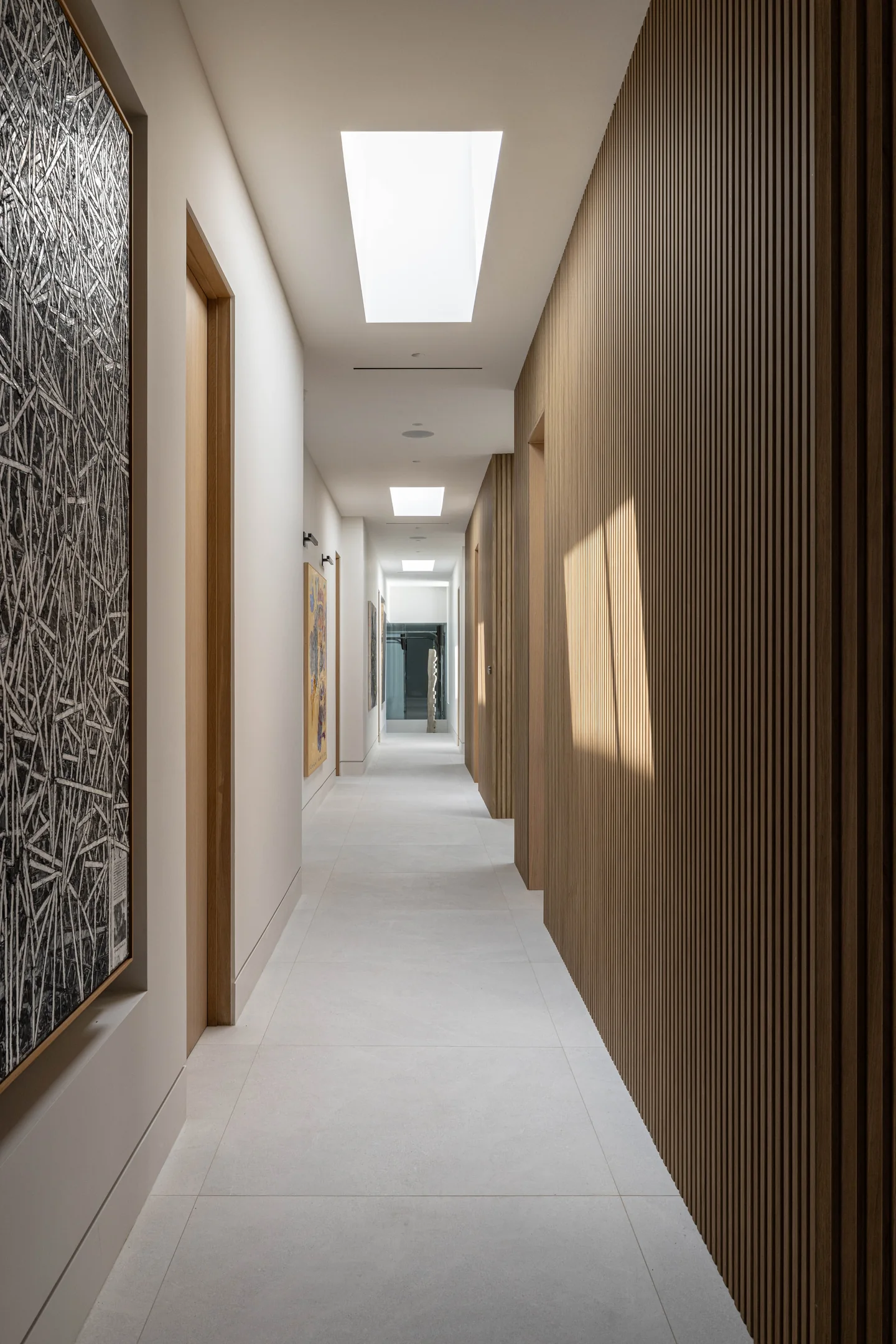 Narrow hallway with timber wall panels and a sequence of rooflights leading to a glazed garden door.