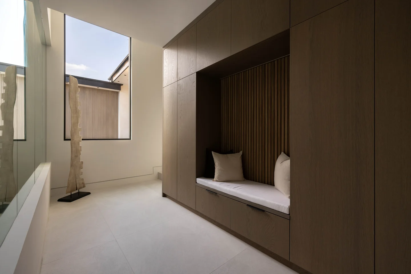 Sheltered courtyard with a recessed built-in bench, timber wall panels and a tall window.
