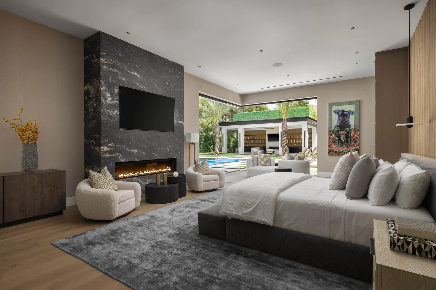 Primary bedroom with a dark stone fireplace, timber wall panels and wide doors opening to the pool garden.