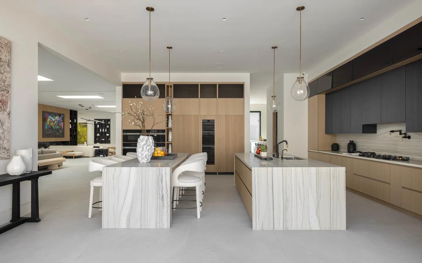 Two kitchen islands face a wall of timber cabinetry and built-in ovens beneath suspended lights.