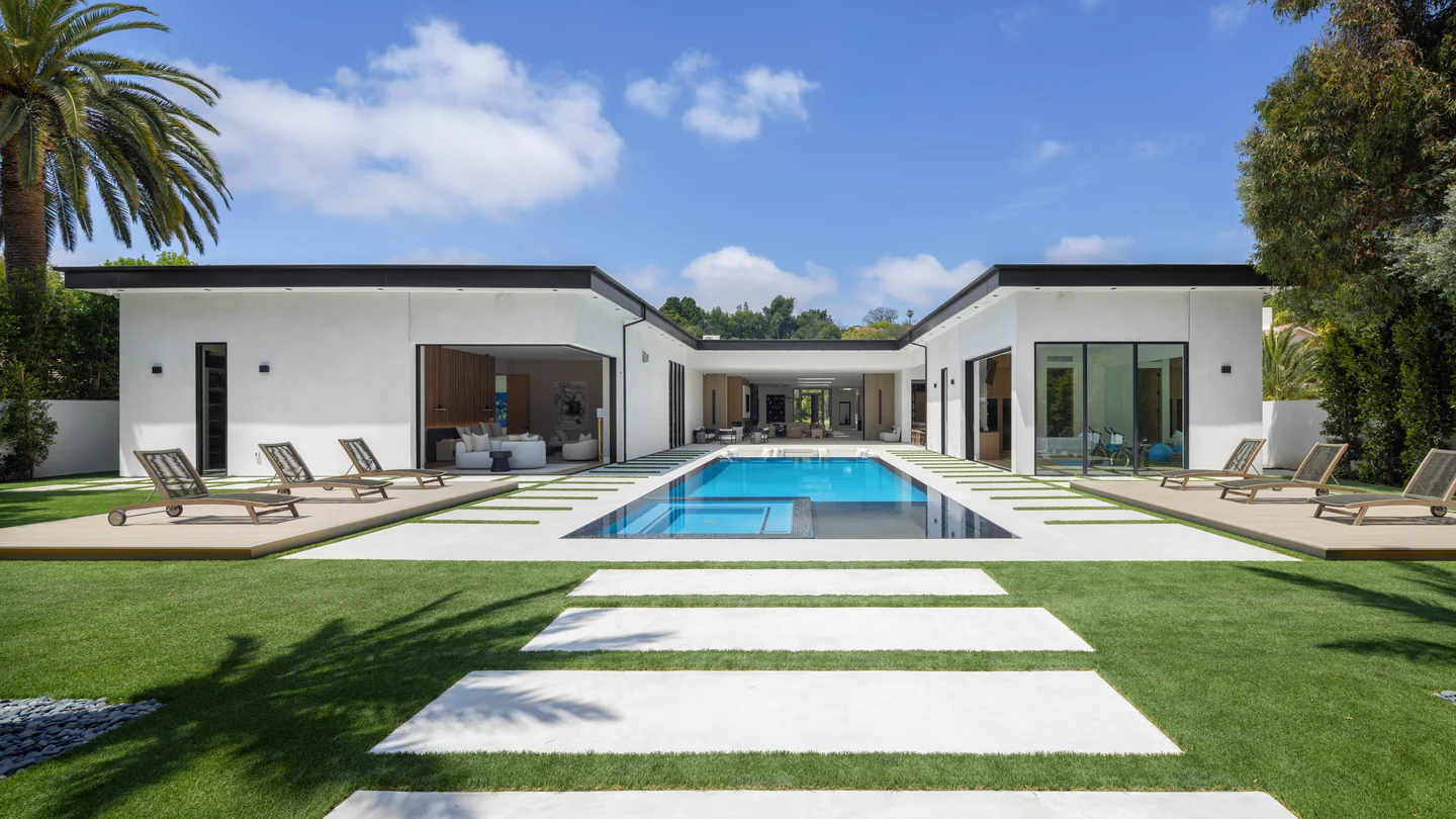 Daylight view across the pool and lawn toward the single-storey rear facade and covered pavilion.