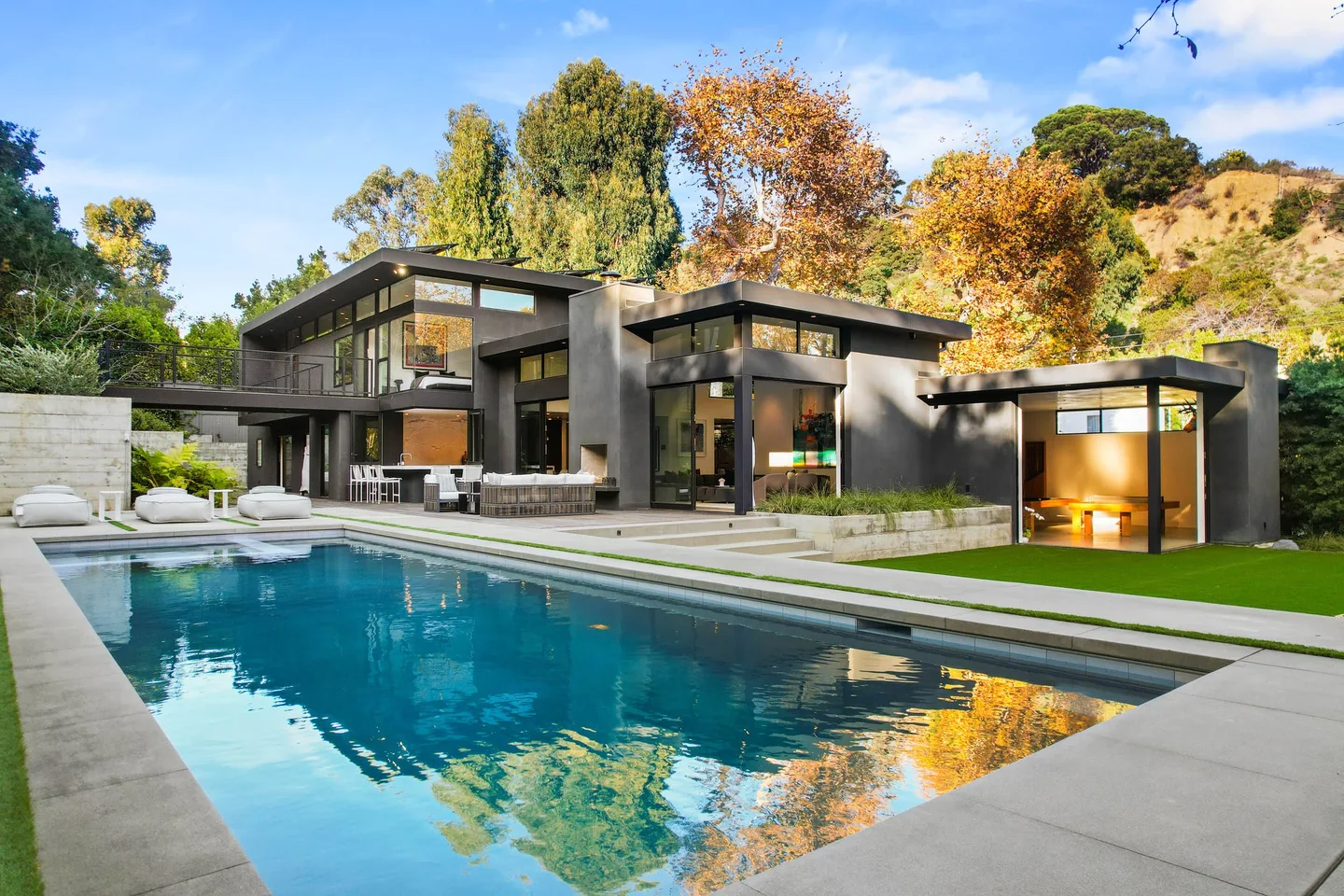 Rivas Canyon residence with dark cladding, a pool, lawn and planted hillside.