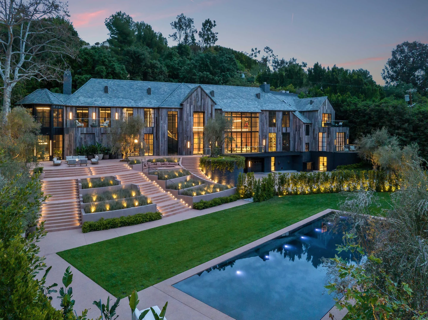 Benedict Canyon Drive: Benedict Canyon residence at dusk, with pitched roofs, tall windows, terraced garden steps and a long pool.
