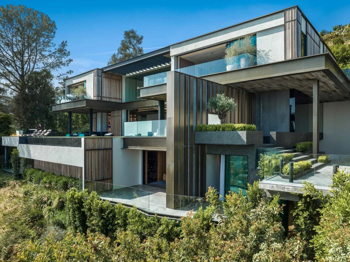 Saint Ives residence with stacked terraces, glass balustrades and dark vertical fins above a planted hillside.