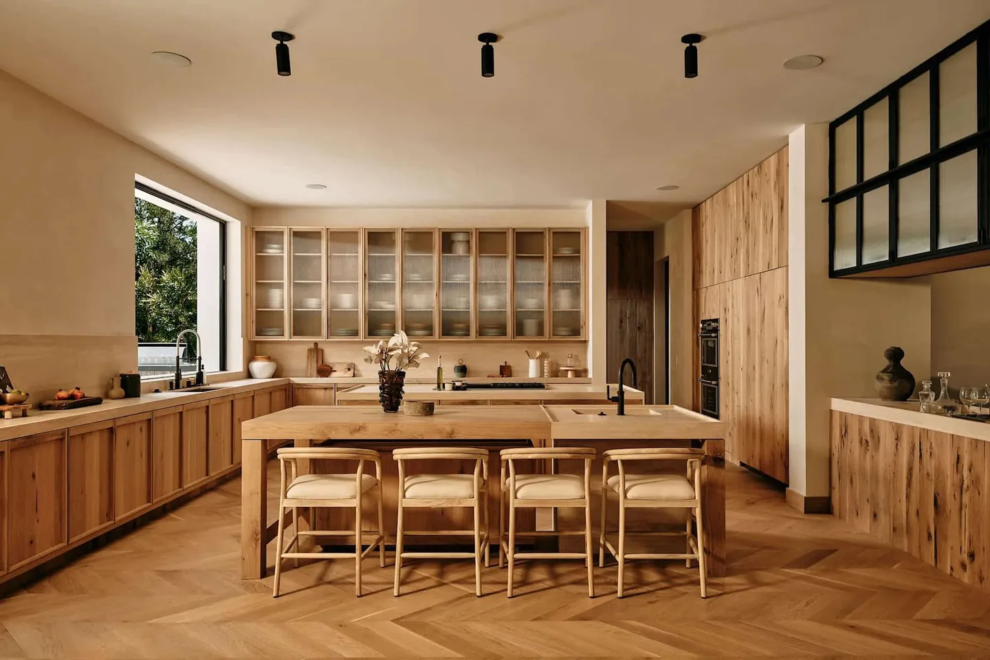 Dobbins kitchen with warm timber cabinetry, an island, herringbone flooring and a dark-framed glazed partition.