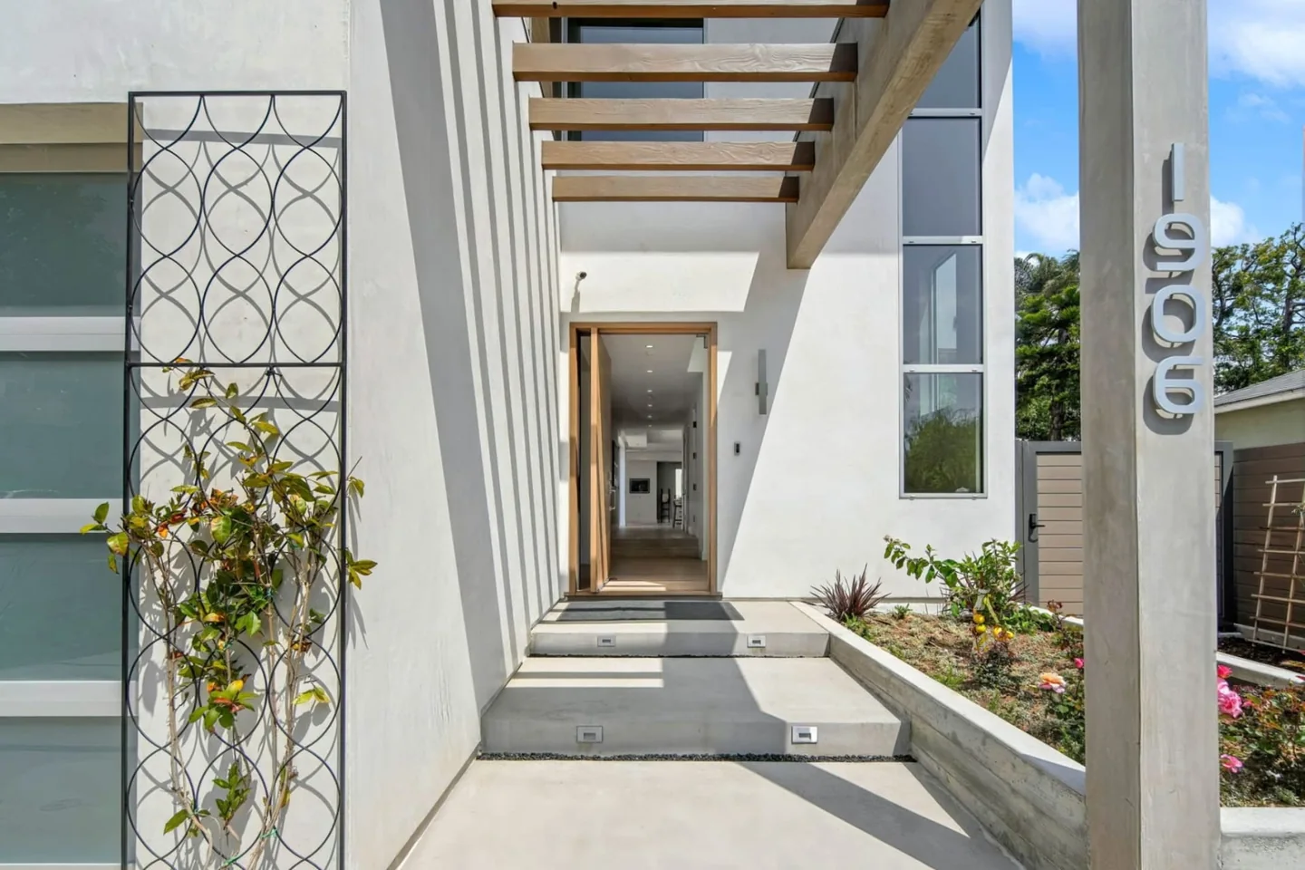 Tall white entry at Fairburn with a recessed timber door, overhead beams and a curved dark screen beside the approach.