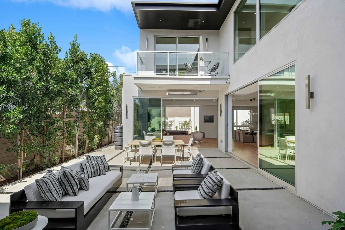 Paved Fairburn courtyard with seating beneath an upper balcony, bordered by wide glazed openings on two levels.