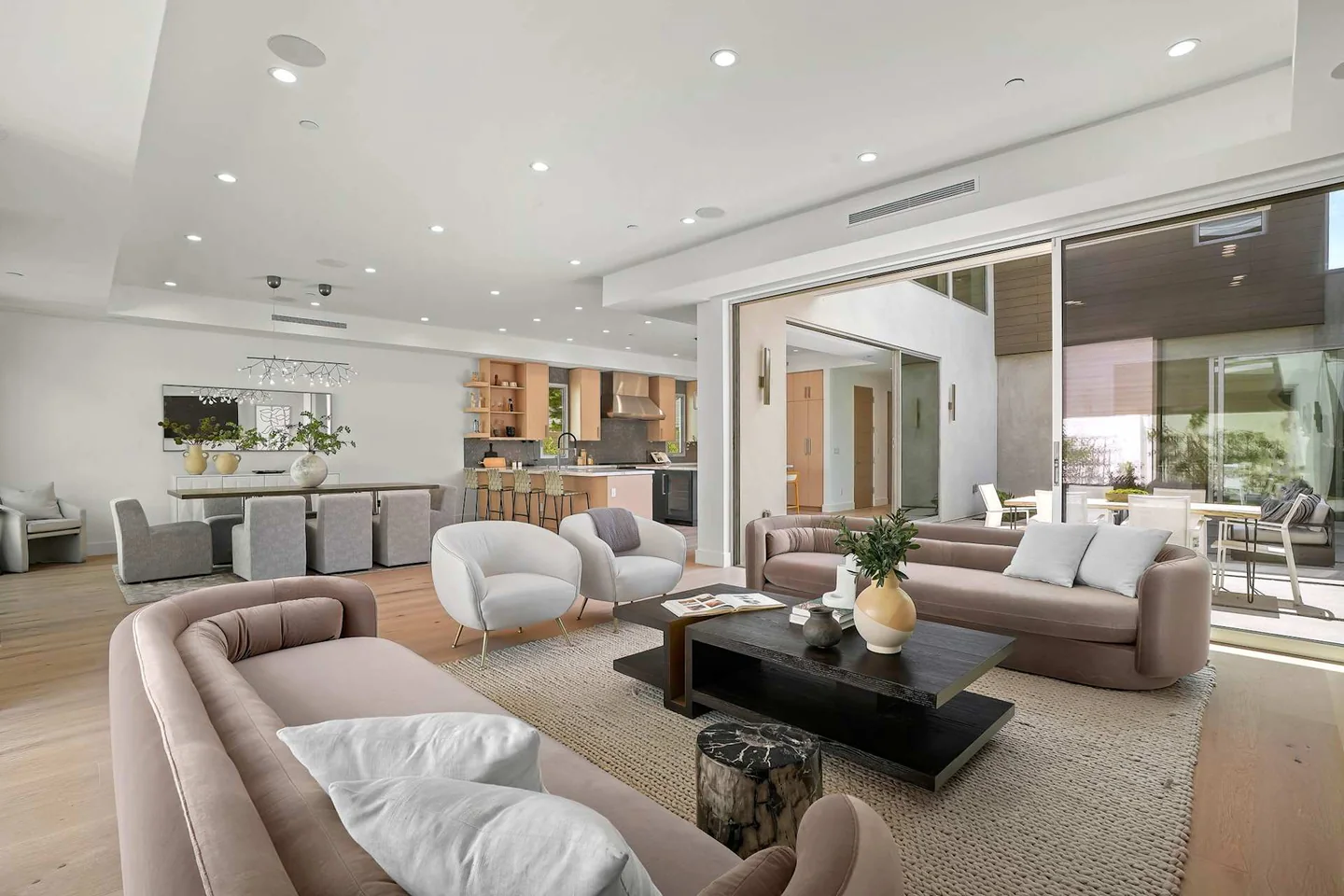 Fairburn living and dining rooms with pale timber floors, warm cabinetry and a broad opening to a planted courtyard.