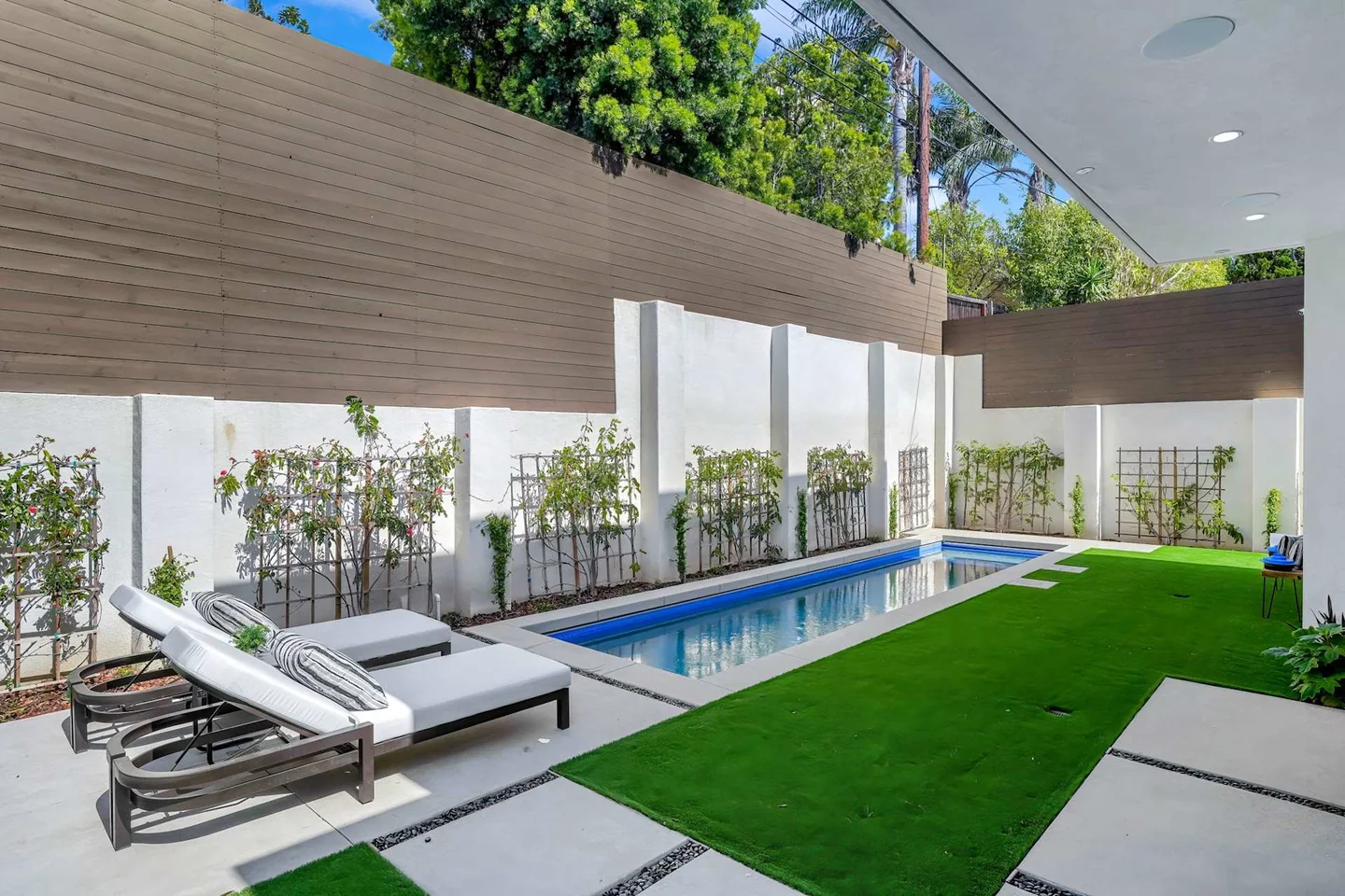 Rectangular Fairburn pool beside a planted boundary wall, with a narrow lawn, pale paving and loungers.
