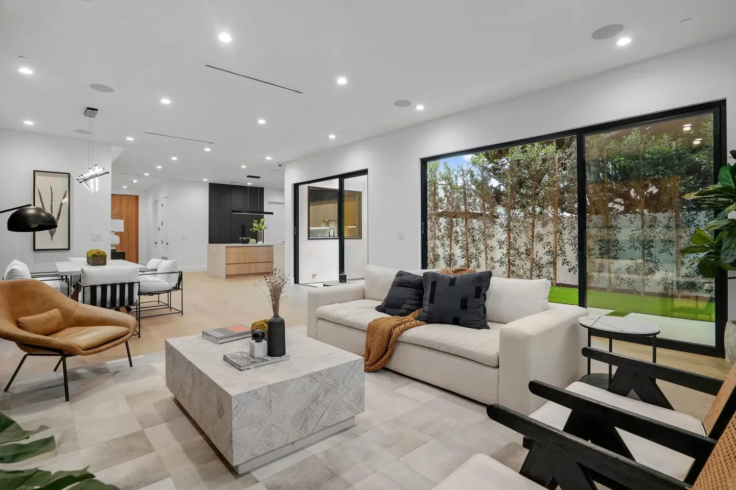 Nowita living room with light timber flooring and broad dark-framed glazing, looking toward the dining area and kitchen.