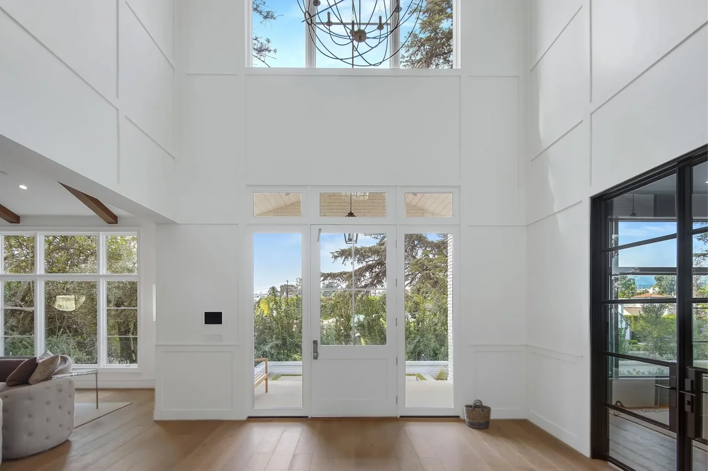 Double-height South Bundy entry with white wall panels, tall dark-framed side glazing and a chandelier above the front doors.