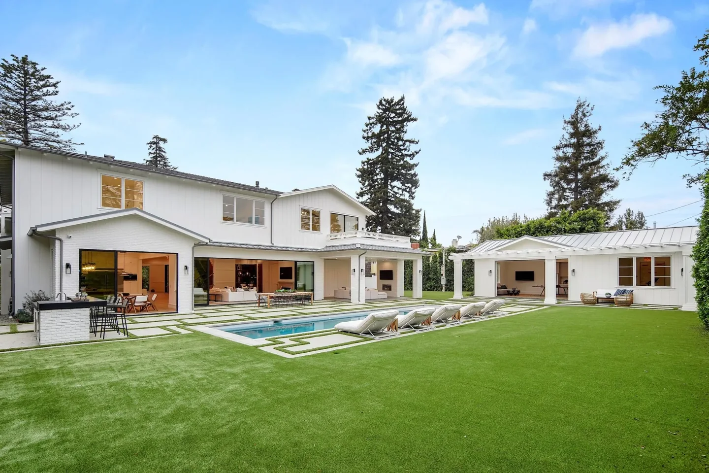 Daylight view of South Bundy Drive showing a white two-story residence, pool, broad lawn and separate garden pavilion.