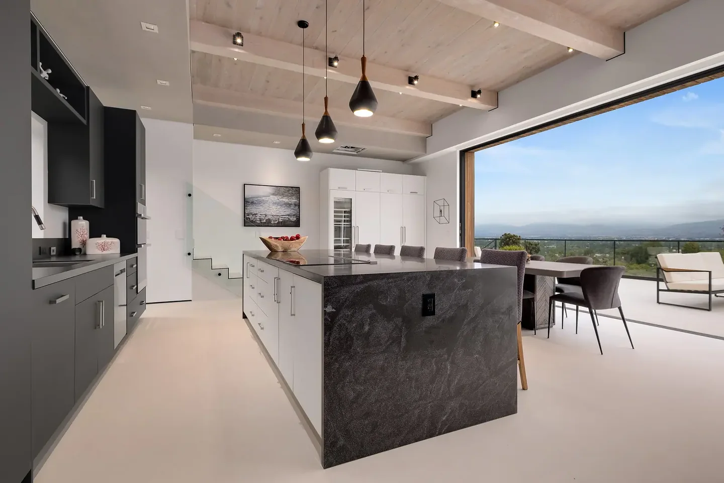 Dixie Canyon kitchen with a dark island, exposed ceiling beams and a broad opening toward the hillside view.