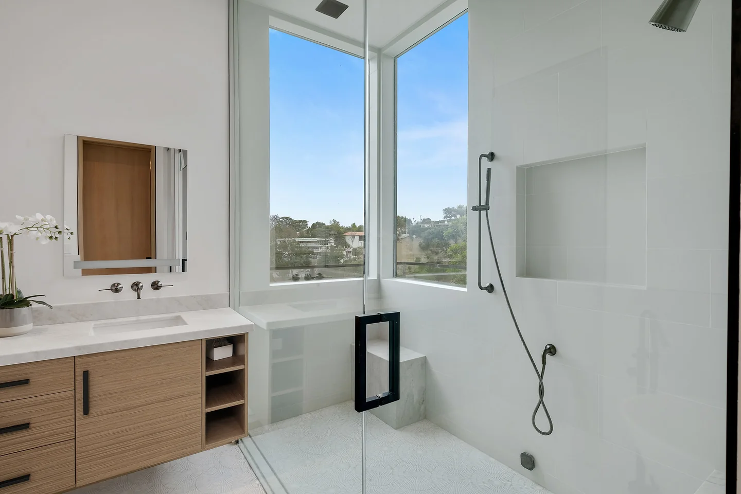 Dixie Canyon bathroom with a timber vanity, pale bath surround and tall glazing to the trees.
