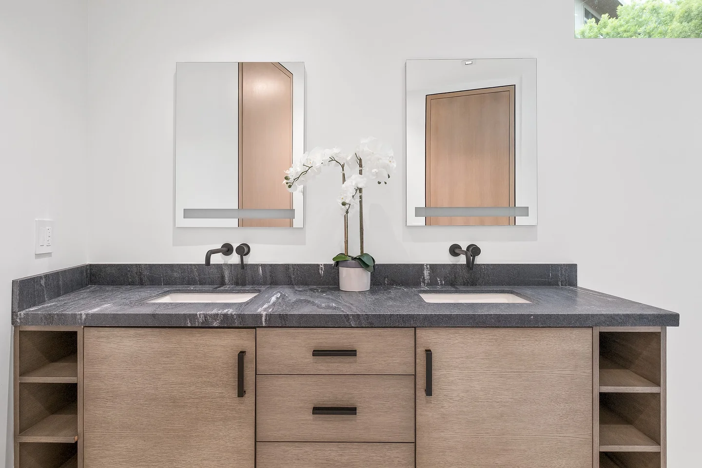 Dixie Canyon double vanity with timber cabinets, a dark counter, twin mirrors and wall-mounted lights.