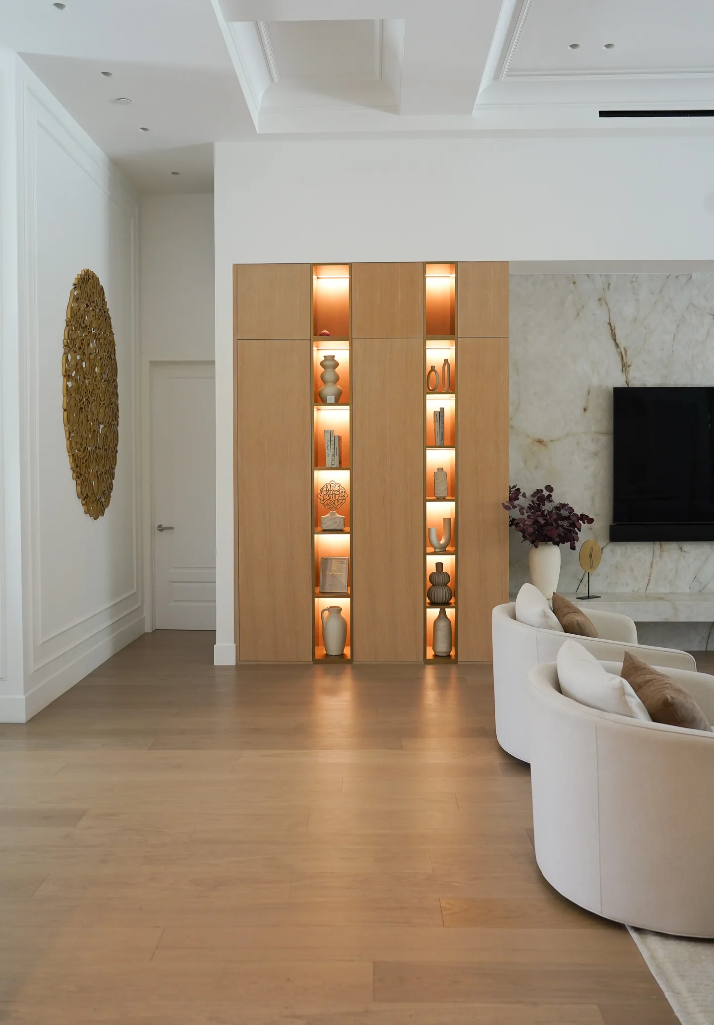 Rio Flora hallway with a veined wall, recessed illuminated display shelves and timber flooring.