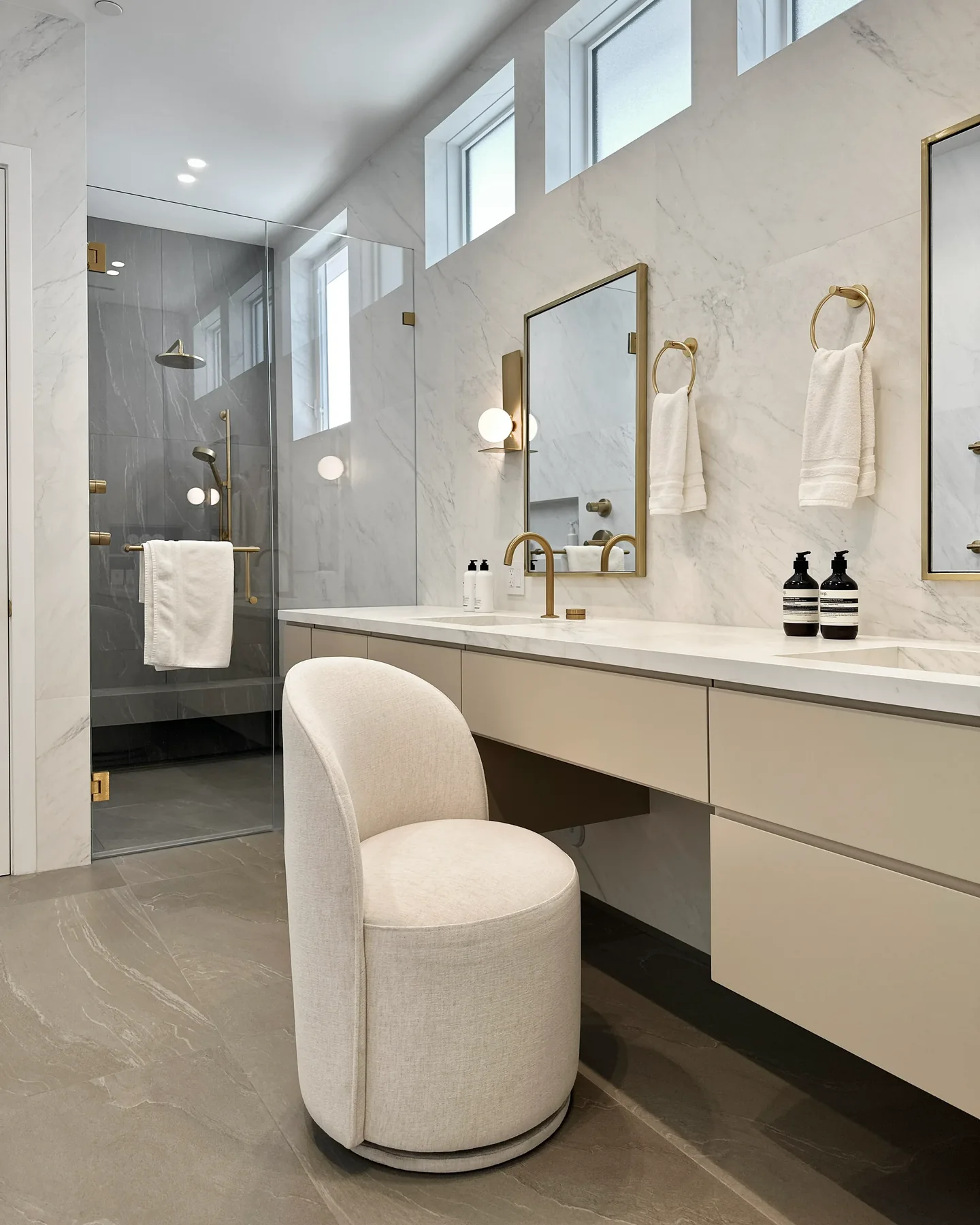 Rio Flora bathroom with a long pale vanity, veined backsplash and multiple wall mirrors beneath high windows.