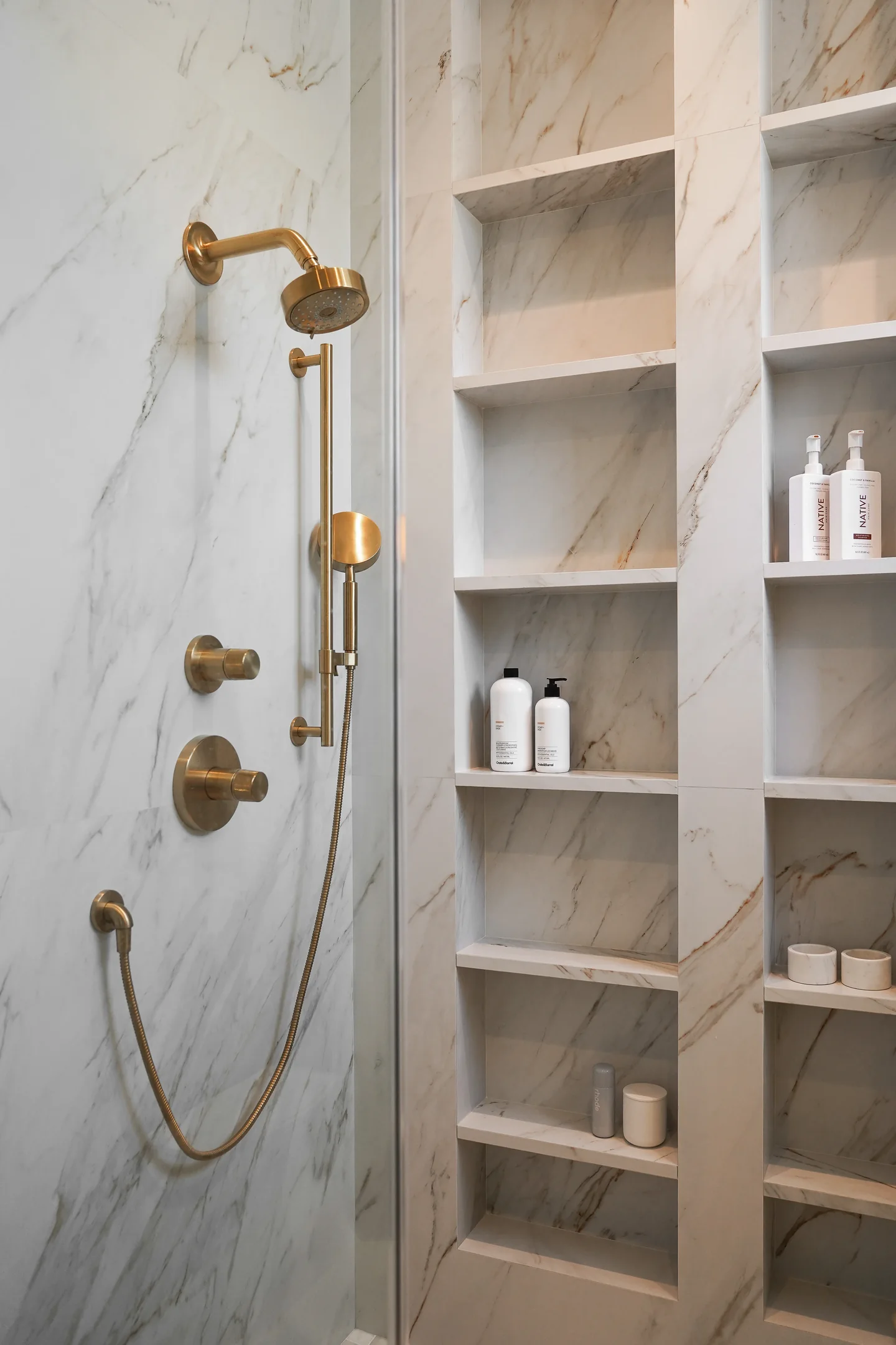 Rio Flora shower with veined wall surfaces, brass-toned fittings and a vertical series of recessed niches.