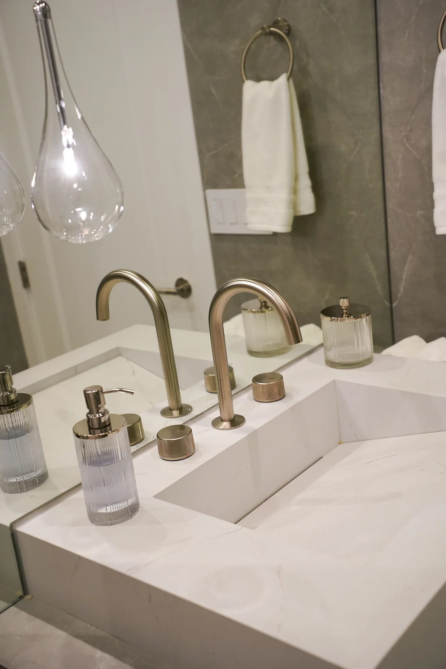 Rio Flora vanity detail with a pale counter, brass-toned taps, an outlined mirror and softly lit wall surfaces.